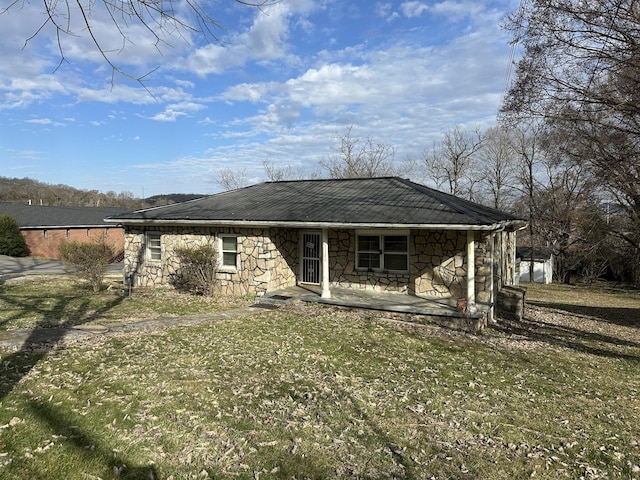 rear view of house with a porch, stone siding, a yard, and metal roof