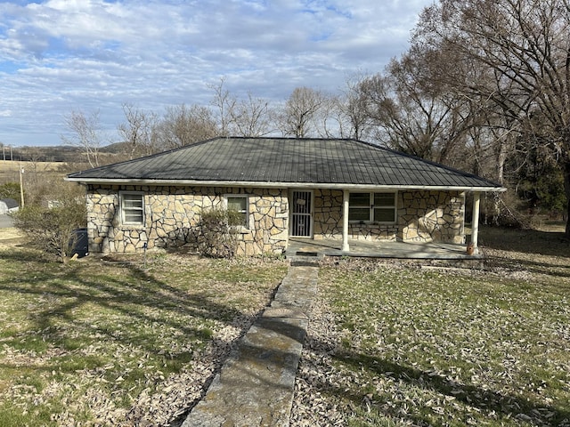 view of front of home featuring covered porch, metal roof, a front lawn, and stone siding