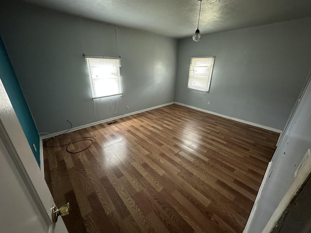 unfurnished room with visible vents, wood finished floors, a wealth of natural light, and baseboards