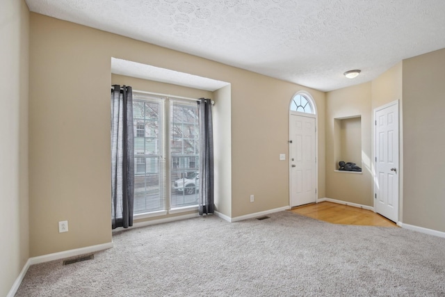 carpeted foyer featuring visible vents, a textured ceiling, and baseboards