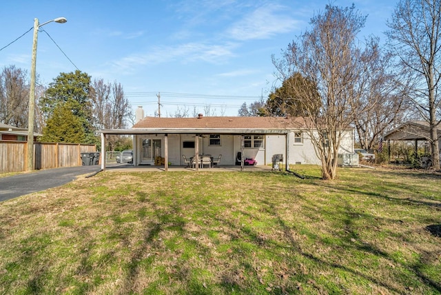 back of house with fence, a lawn, a carport, a chimney, and a patio area