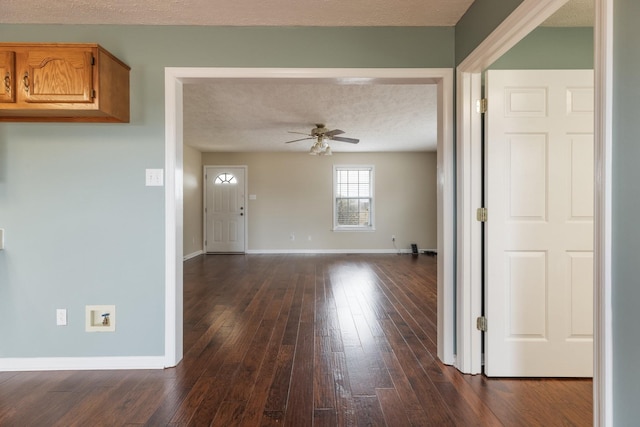 interior space with a textured ceiling, ceiling fan, dark wood-type flooring, and baseboards