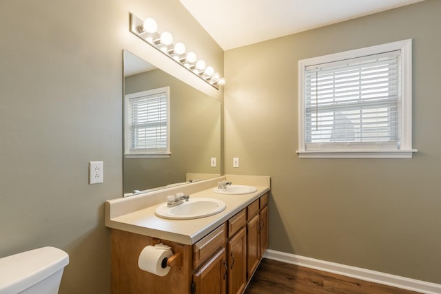 bathroom featuring toilet, double vanity, baseboards, and a sink