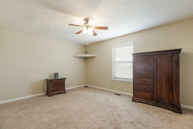 unfurnished bedroom with a textured ceiling, light colored carpet, a ceiling fan, baseboards, and visible vents