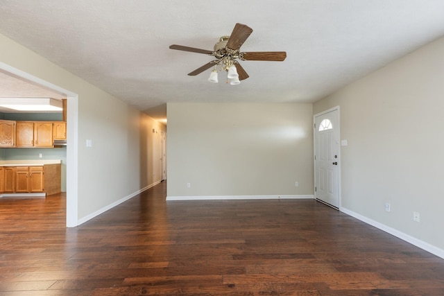 unfurnished living room with dark wood-style flooring, a ceiling fan, and baseboards