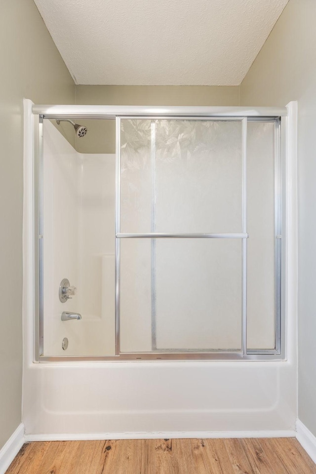 full bathroom with combined bath / shower with glass door, a textured ceiling, baseboards, and wood finished floors