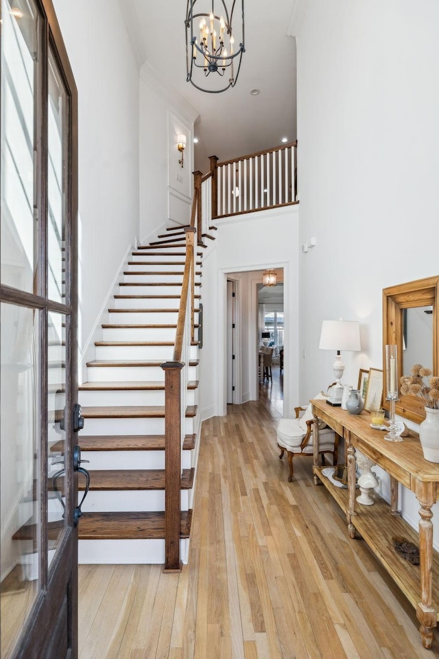 foyer entrance with light wood-style flooring, a notable chandelier, a towering ceiling, stairway, and crown molding