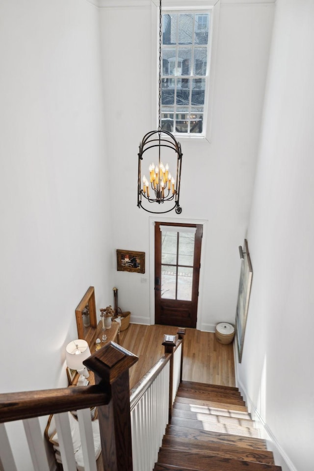 stairway with a chandelier, a towering ceiling, and wood finished floors