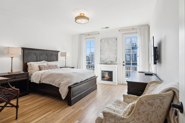 bedroom with visible vents, a glass covered fireplace, ornamental molding, access to outside, and light wood-style floors