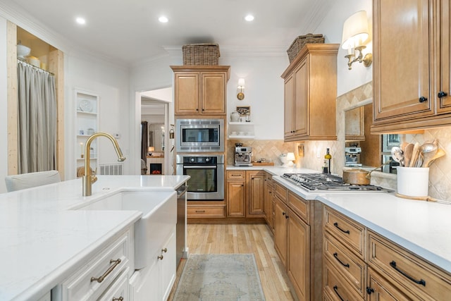 kitchen with stainless steel appliances, light countertops, ornamental molding, a sink, and light wood-type flooring