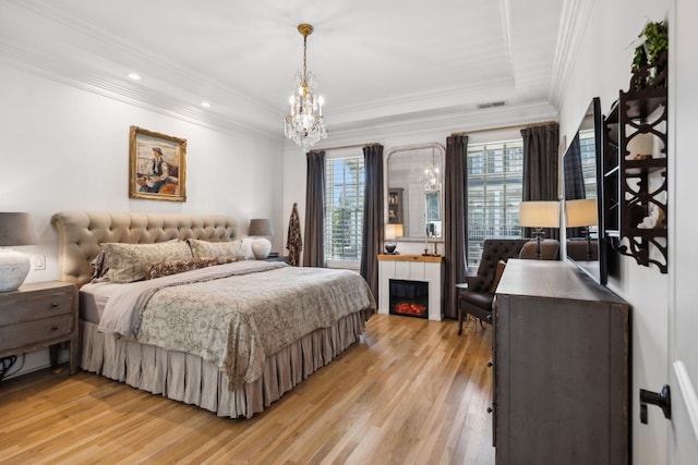 bedroom with a chandelier, a large fireplace, visible vents, light wood-type flooring, and crown molding