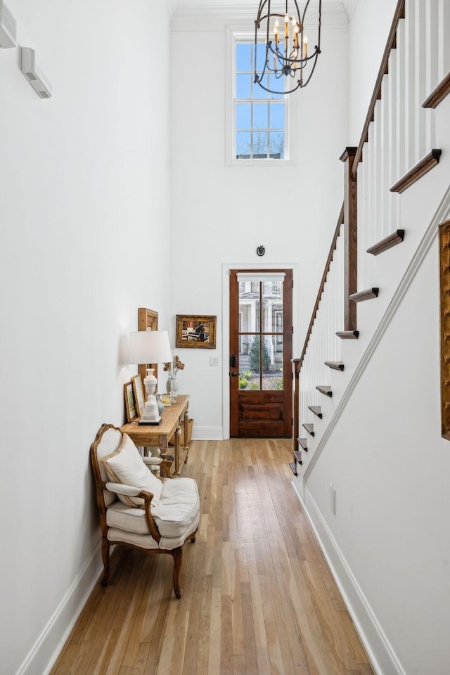 foyer entrance with stairs, light wood finished floors, a towering ceiling, and baseboards