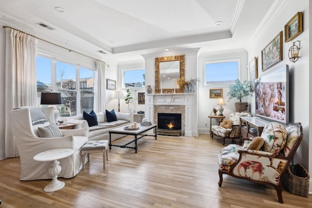 living area with a tray ceiling, a lit fireplace, visible vents, and light wood-style flooring