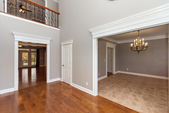 empty room featuring french doors, crown molding, an inviting chandelier, wood finished floors, and baseboards