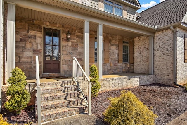 property entrance featuring stone siding, a porch, roof with shingles, and brick siding