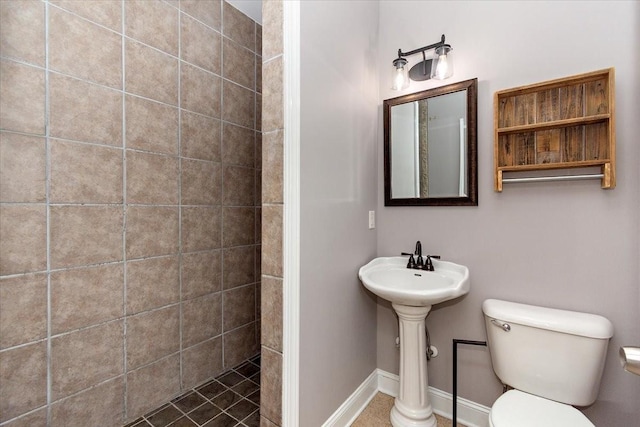 full bathroom with baseboards, tiled shower, a sink, and toilet