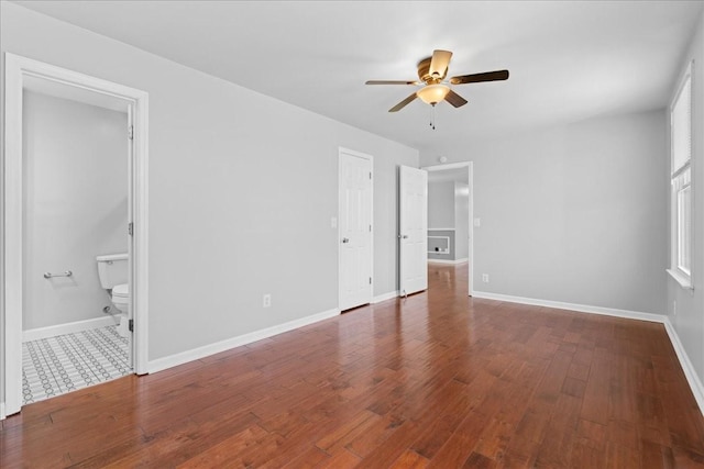 unfurnished bedroom featuring ceiling fan, connected bathroom, baseboards, and hardwood / wood-style flooring