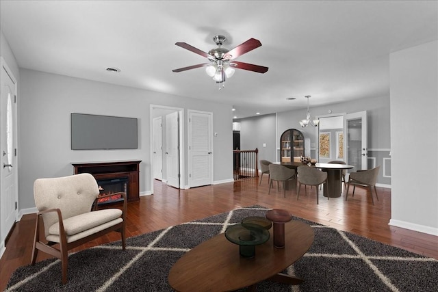 living room with visible vents, baseboards, a glass covered fireplace, wood finished floors, and ceiling fan with notable chandelier