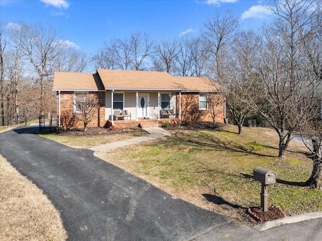 ranch-style home with driveway, covered porch, brick siding, and a front yard