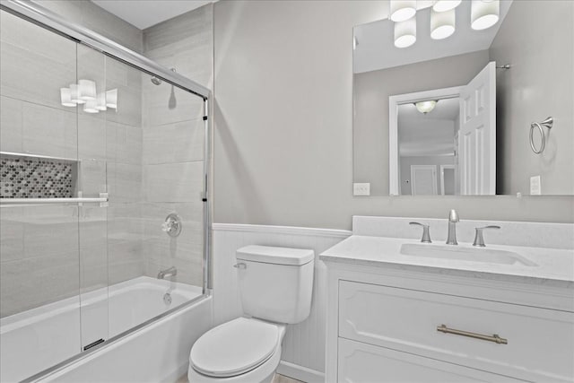 bathroom with a wainscoted wall, combined bath / shower with glass door, vanity, and toilet