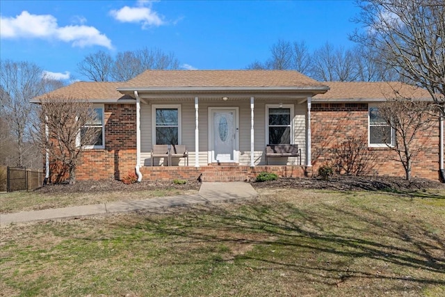 ranch-style house with a porch, a front yard, brick siding, and a shingled roof