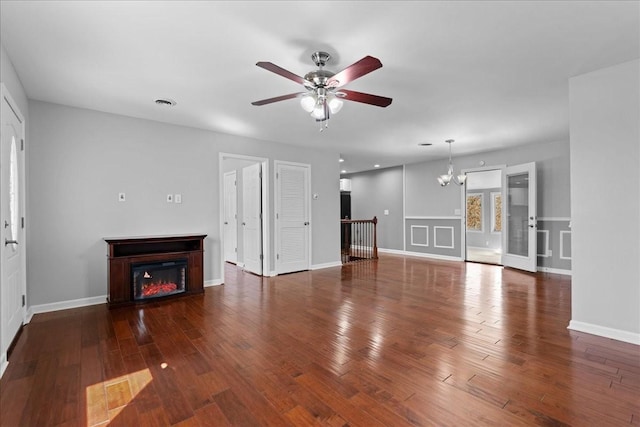 unfurnished living room featuring visible vents, wood finished floors, a lit fireplace, baseboards, and ceiling fan with notable chandelier