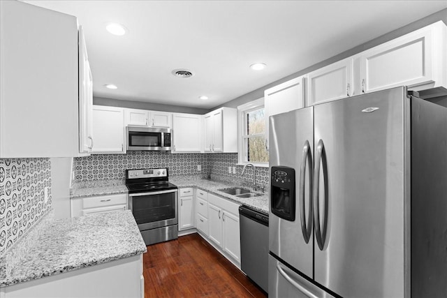 kitchen with light stone counters, stainless steel appliances, visible vents, white cabinetry, and a sink