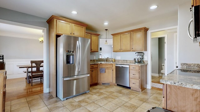 kitchen with stainless steel appliances, wainscoting, a sink, and light stone countertops