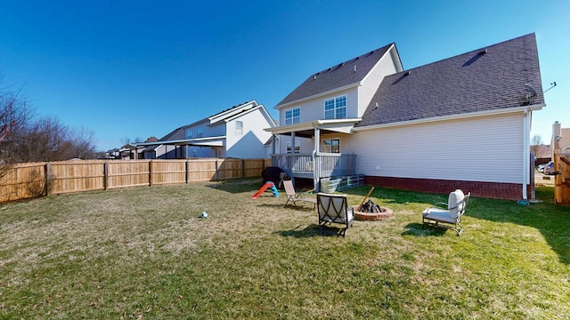 back of house with a fenced backyard, a fire pit, roof with shingles, and a yard