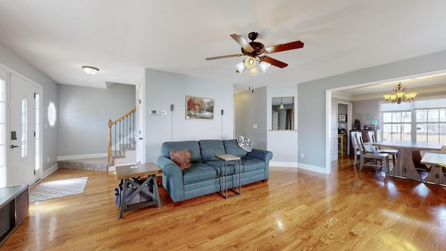 living room with light wood-style floors, stairs, baseboards, and ceiling fan with notable chandelier