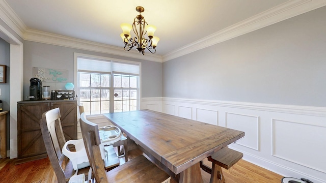 dining area with light wood finished floors, crown molding, a notable chandelier, and a wainscoted wall