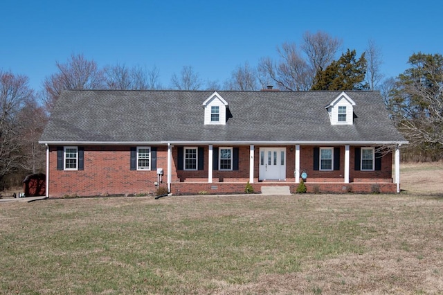 cape cod house featuring covered porch, roof with shingles, a front lawn, and brick siding