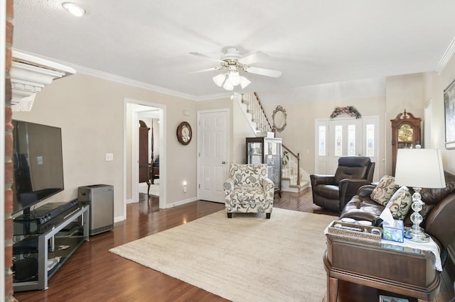 living area with baseboards, a ceiling fan, dark wood-style flooring, stairs, and crown molding