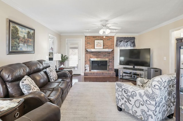 living area featuring ceiling fan, a brick fireplace, wood finished floors, and crown molding