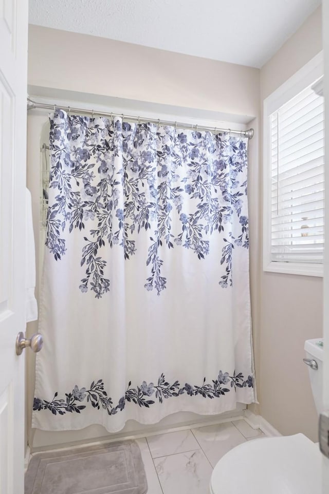 full bathroom featuring marble finish floor, shower / bath combo, and toilet