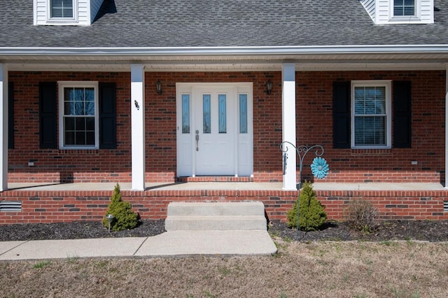 doorway to property featuring covered porch, a shingled roof, and brick siding