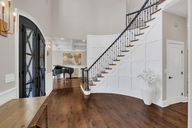 entryway with coffered ceiling, a decorative wall, wood finished floors, and beamed ceiling