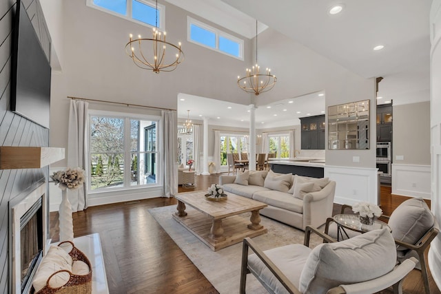 living room featuring recessed lighting, a fireplace, a towering ceiling, dark wood-style floors, and an inviting chandelier