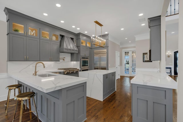 kitchen with a peninsula, a sink, appliances with stainless steel finishes, gray cabinets, and custom exhaust hood