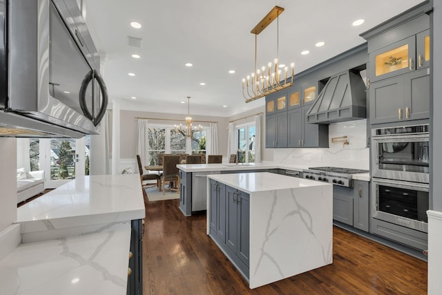 kitchen with a chandelier, gray cabinetry, a peninsula, stainless steel appliances, and wall chimney exhaust hood