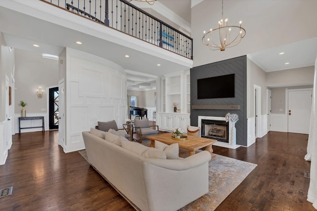 living room featuring a decorative wall, a large fireplace, dark wood-type flooring, a towering ceiling, and ornamental molding