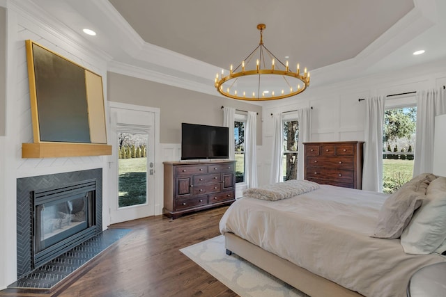 bedroom featuring dark wood-style floors, a tray ceiling, a decorative wall, a large fireplace, and access to outside