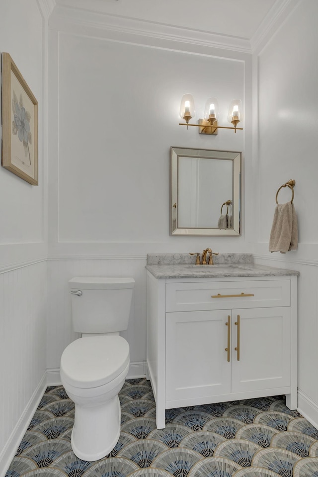 half bathroom featuring toilet, ornamental molding, a decorative wall, and vanity