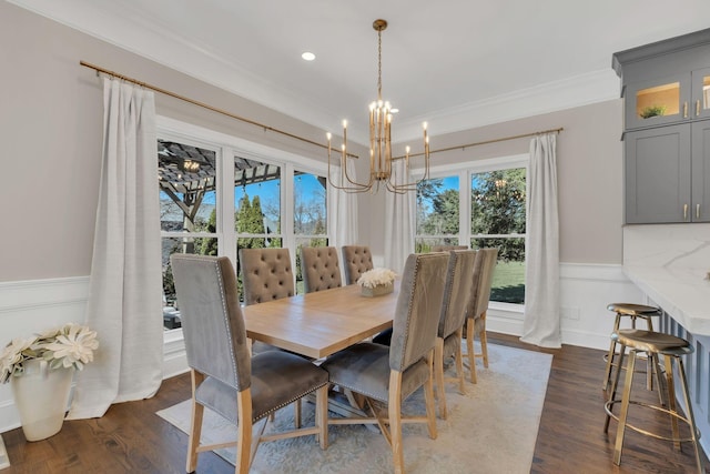 dining space featuring dark wood-type flooring, wainscoting, crown molding, and an inviting chandelier