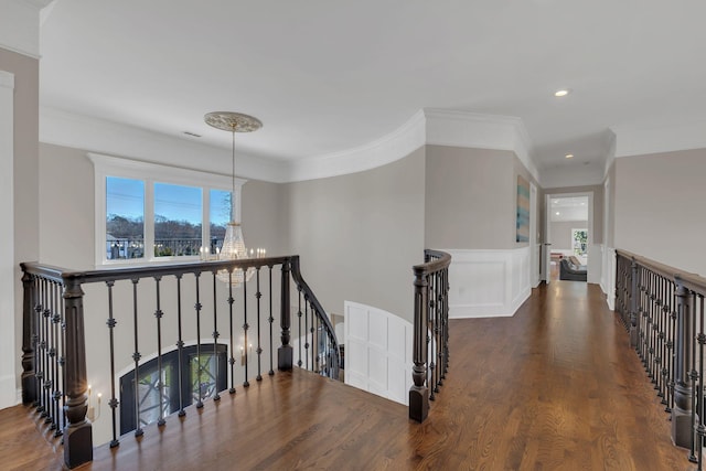 corridor featuring a chandelier, wood finished floors, an upstairs landing, ornamental molding, and wainscoting