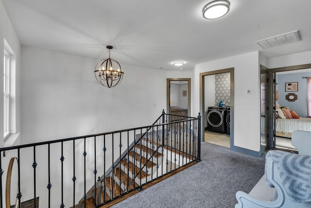 hallway featuring a chandelier, carpet flooring, visible vents, an upstairs landing, and washer and clothes dryer