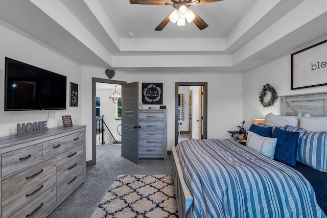 carpeted bedroom with a tray ceiling and ceiling fan with notable chandelier