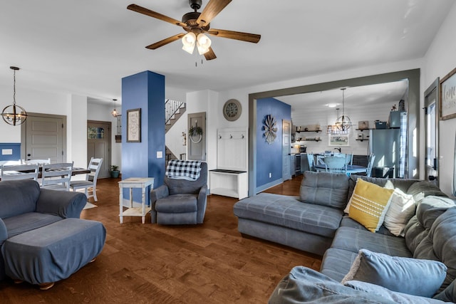 living area featuring stairway, dark wood-type flooring, and ceiling fan with notable chandelier