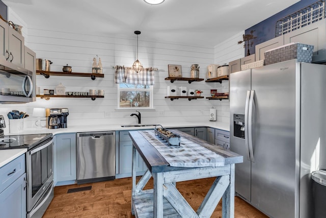 kitchen with wood finished floors, stainless steel appliances, light countertops, open shelves, and a sink