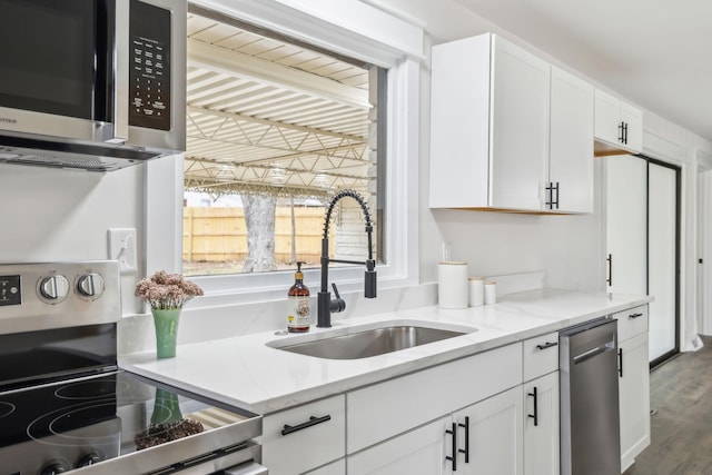 kitchen with wood finished floors, appliances with stainless steel finishes, a sink, and white cabinets